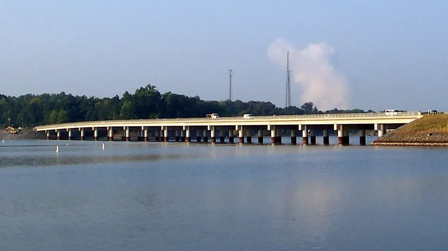 The long, low Buster Boyd Bridge crossing Lake Wylie on concrete piers, with a wooded shoreline and a white steam plume in the distance